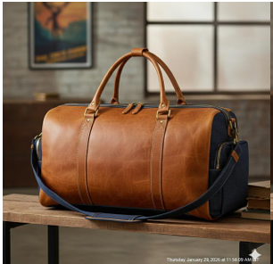 Tan full-grain leather weekender duffle with navy denim base on a wooden table in warm interior light